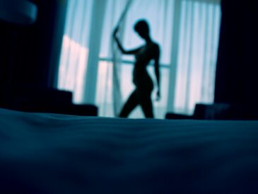 sillouehtte photo of woman standing beside window curtains