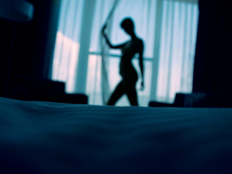sillouehtte photo of woman standing beside window curtains